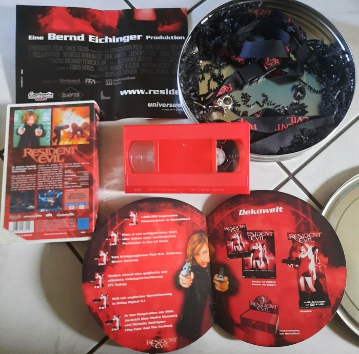 Open box with two lanyards and paper strips, folded poster, VHS case and tape, and open booklet